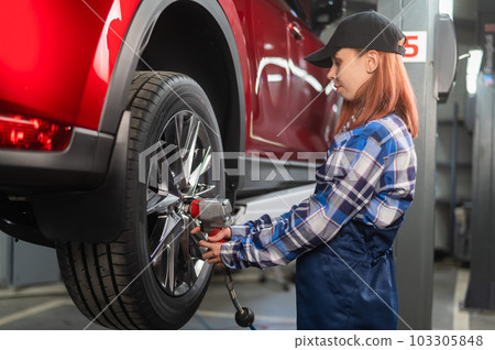 Woman mechanic uses pneumatic wrench to tighten the wheel nut. Girl at men's work.  103305848