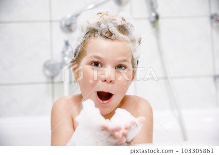 Cute child with shampoo foam and bubbles on hair taking bath. Portrait of happy smiling preschool girl health care and hygiene concept. Washes hair by herself. 103305861