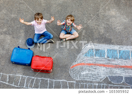Two little kids boys having fun with train picture drawing with colorful chalks on asphalt. Children having fun with chalk and crayon painting. going on vacations and travel. Friends with suitcases Two little kids boys having fun with train picture drawing with colorful chalks on asphalt. Children having fun with chalk and crayon painting. going on vacations and travel. Friends with suitcases 103305932