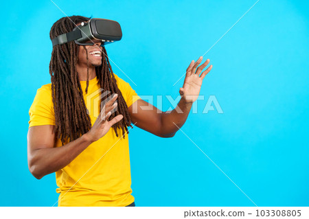 Happy latin man with dreadlocks wearing Virtual Reality goggles 103308805