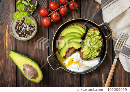 Healthy breakfast, sandwich with avocado and egg. Wholemeal bread toast sliced avocado and poached egg on a rustic table. View from above. 103309059