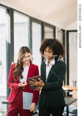 Businesswomen work and discuss their business plans. A Human employee explains and shows her colleague the results paper in modern office.. Businesswomen work and discuss their business plans. A Human employee explains and shows her colleague the results paper in modern office.. 103310111