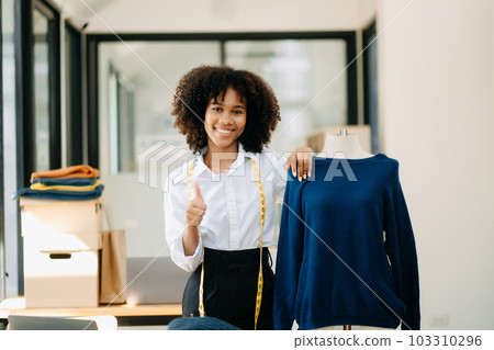 Calm curly brunette dark skinned woman on desk in office of fashion designer and holds tablet and smartphone... 103310296