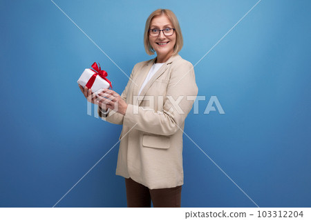 middle-aged business concept. 50s woman in a jacket with a gift on a studio background with copy middle-aged business concept. 50s woman in a jacket with a gift on a studio background with copy 103312204