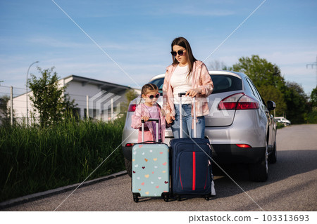 Mom and daughter stand near the car with their suitcases and waiting for the trip. Family journey Mom and daughter stand near the car with their suitcases and waiting for the trip. Family journey 103313693