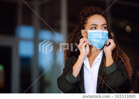 Portrait of brunette woman in sterile medical mask on her face looking at camera outdoors close up. Portrait of brunette woman in sterile medical mask on her face looking at camera outdoors close up. 103313885