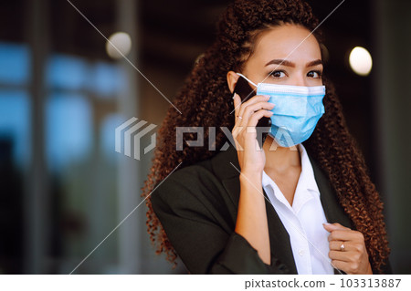 Portrait of a business woman wearing a protective mask with phone solves work issues. Covid-2019. Portrait of a business woman wearing a protective mask with phone solves work issues. Covid-2019. 103313887