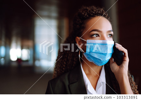 Portrait of a business woman wearing a protective mask with phone solves work issues. Covid-2019. 103313891