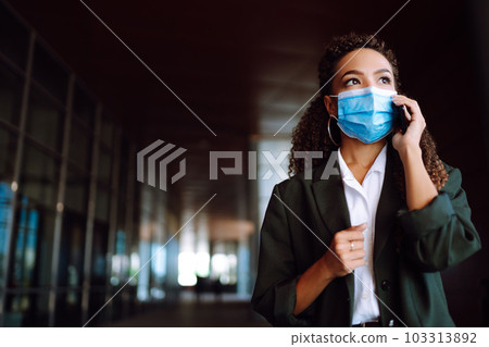 Portrait of a business woman wearing a protective mask with phone solves work issues. Covid-2019. 103313892