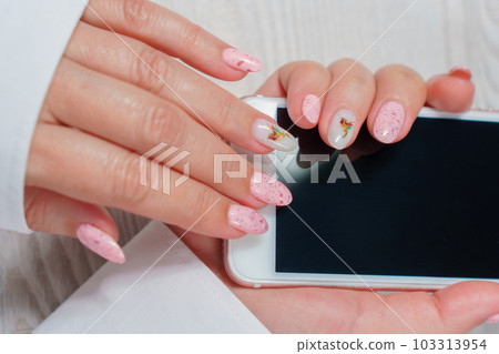 Women's hands with pink manicure are holding a white smartphone with an empty screen. Women's hands with pink manicure are holding a white smartphone with an empty screen. 103313954