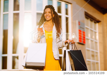 Young woman with shopping bags walking on street. Sale, shopping and happy people concept. 103314109