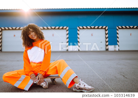 Beautiful African American woman posing with a skateboard. Hipster woman with curly hair with skateboard at sunset. Beautiful African American woman posing with a skateboard. Hipster woman with curly hair with skateboard at sunset. 103314639