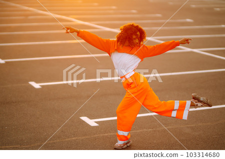 Young African American woman - dancer dancing in the street at sunset. Stylish woman with curly hair in an orange suit showing some moves. Young African American woman - dancer dancing in the street at sunset. Stylish woman with curly hair in an orange suit showing some moves. 103314680