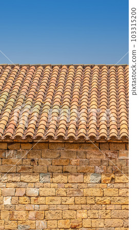 stone wall of a house with a red roof and blue sky 103315200