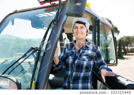 Confident female farm owner driving tractor 103315449