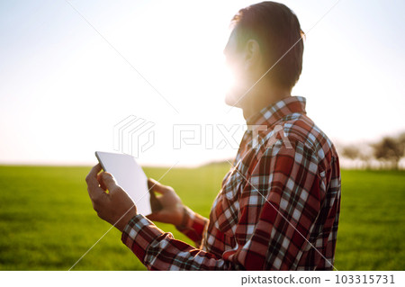 Farmer working with digital tablet in field at sunset. Checking wheat field. Agriculture concept. 103315731