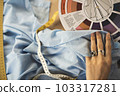 A female fashion designer holds flower samples in her hands, choosing a fabric of blue shades of textiles in the workplace, a dressmaker or tailor, hands close-up view 103317281