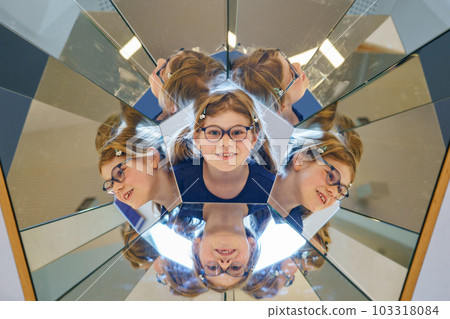 Little child playing with mirrors. Happy preschool girl with glasses having fun with experiments, indoors. 103318084