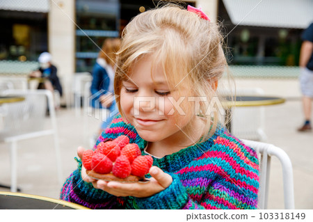 Adorable little girl and delicious raspberry cake. Preschool child eating sweet dessert in French outdoor cafe. 103318149