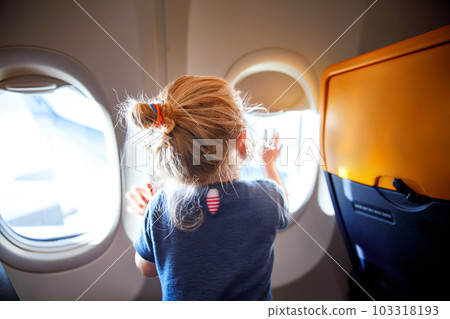 Adorable little girl traveling by an airplane. Child sitting by aircraft window and looking outside. Traveling with kids abroad. Family on summer vacations. Adorable little girl traveling by an airplane. Child sitting by aircraft window and looking outside. Traveling with kids abroad. Family on summer vacations. 103318193