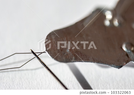 Sewing needle threader tool in use and a single black string.  103322063