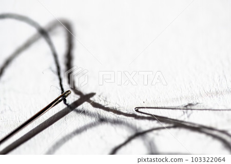 Sewing needle threader tool in use and a single black string.  103322064