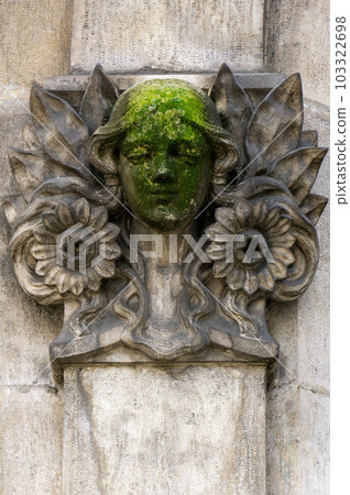 Bas-relief - mascaron in the form of a girl's face surrounded by flowers and leaves 103322698