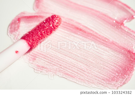 Smears of shining lip gloss and lip gloss brush on white background, hard shadows 103324382
