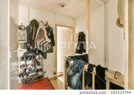 a room with clothes hanging on the wall and an open door that leads to another room in which is white 103324744