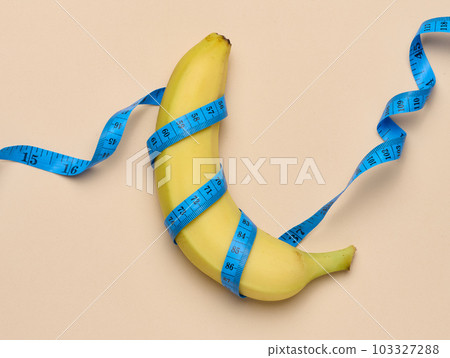 Ripe yellow banana wrapped in a measuring tape, weight loss concept, top view 103327288