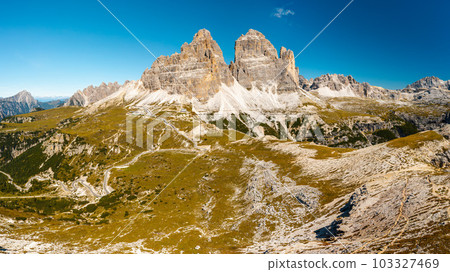Mountainous terrain at sunrise. Majestic Three Peaks of Lavaredo with sand-covered foothills in Alps at beginning of sunny day aerial view in back lit Mountainous terrain at sunrise. Majestic Three Peaks of Lavaredo with sand-covered foothills in Alps at beginning of sunny day aerial view in back lit 103327469