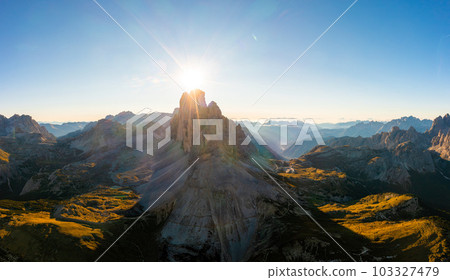 Mountain landscape of Tre Cime di Lavaredo at sunrise. Rocky ranges and wide highland valleys in Alps under clear sky aerial view in back lit Mountain landscape of Tre Cime di Lavaredo at sunrise. Rocky ranges and wide highland valleys in Alps under clear sky aerial view in back lit 103327479