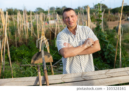 Positive adult man standing near wooden fence in homestead 103328161