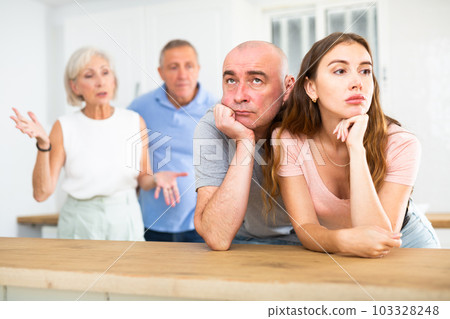 Husband and wife listen to their parents scold them in home kitchen Husband and wife listen to their parents scold them in home kitchen 103328248