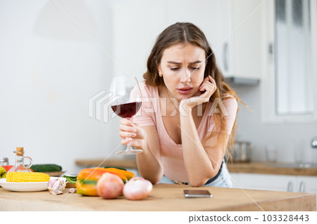 Upset woman texting on mobile phone in kitchen Upset woman texting on mobile phone in kitchen 103328443