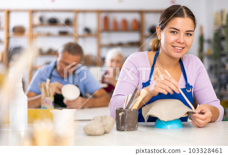 Woman using spatula and a knife creates dishes from soft clay 103328461