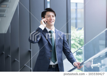 一位英俊的亞洲(日本)商人,穿著西裝,打電話給商業場景 一位英俊的亞洲(日本)商人,穿著西裝,打電話給商業場景 103330427