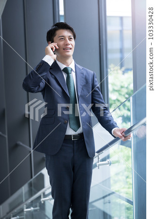 一位英俊的亞洲(日本)商人,穿著西裝,打電話給商業場景 一位英俊的亞洲(日本)商人,穿著西裝,打電話給商業場景 103330428