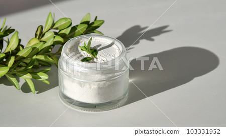 An open jar of facial scrub powder with a green sprig. An open jar of facial scrub powder with a green sprig. 103331952