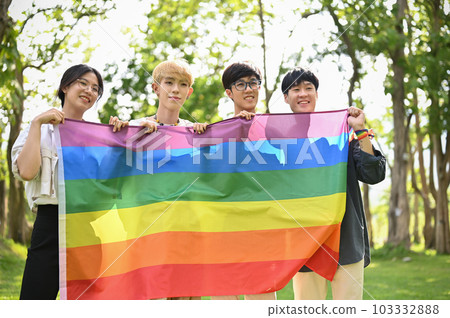A group of young Asian college friends are holding a rainbow LGBTQ flag outdoors. 103332888