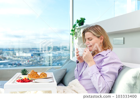 Happy middle aged, beautiful woman having breakfast, relaxing in hotel bed, luxury apartments. 103333400