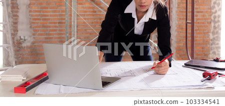 Young caucasian architect woman looking laptop and working drawing blueprint for planning building. 103334541