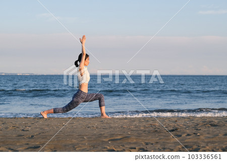 Yoga instructor doing warrior pose on the beach 103336561