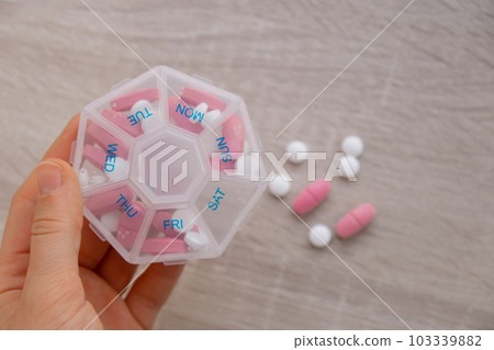 Woman sorting pills Organizer weekly shots Closeup of medical pill box with doses of tablets for daily take medicine with white pink drugs and capsules. Young woman getting her daily vitamins at home 103339882