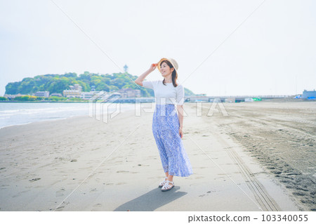 A woman with a straw hat walking on the beach while feeling the sea breeze 103340055