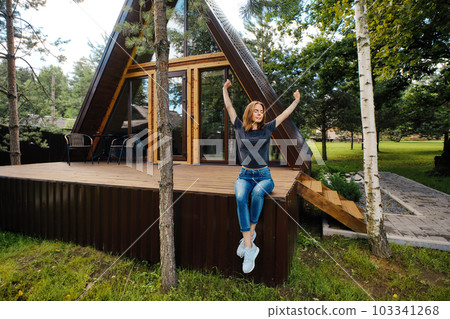 Woman sits on terrace of log cabin in the morning and stretching arms Woman sits on terrace of log cabin in the morning and stretching arms 103341268