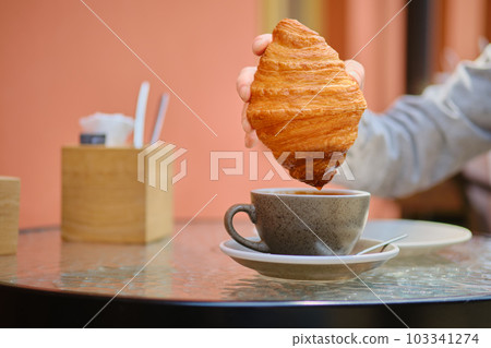 Unrecognizable woman dipping croissant into cappuccino Unrecognizable woman dipping croissant into cappuccino 103341274