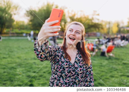 Beautiful woman in casual clothing using her phone on city street. Young hipster taking selfie on nature background. Posing in the street at sunny day. 103346486