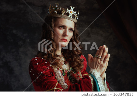 medieval queen in red dress with crown praying 103347035