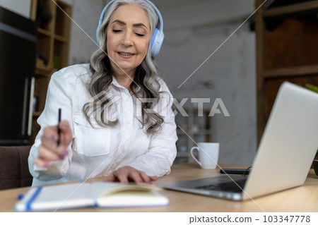 Senior woman in headphones listening an online seminar 103347778